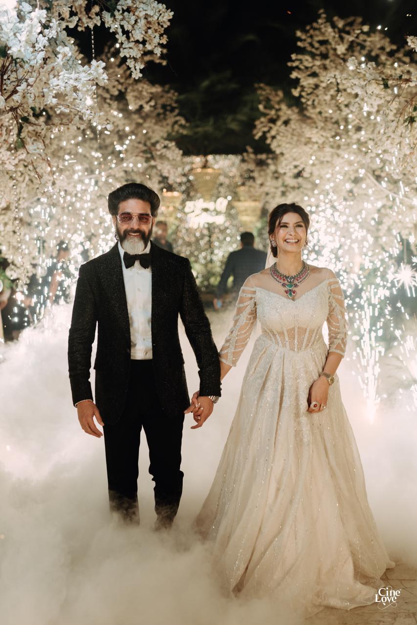 A couple arriving hand in hand beneath a sparkling floral arch